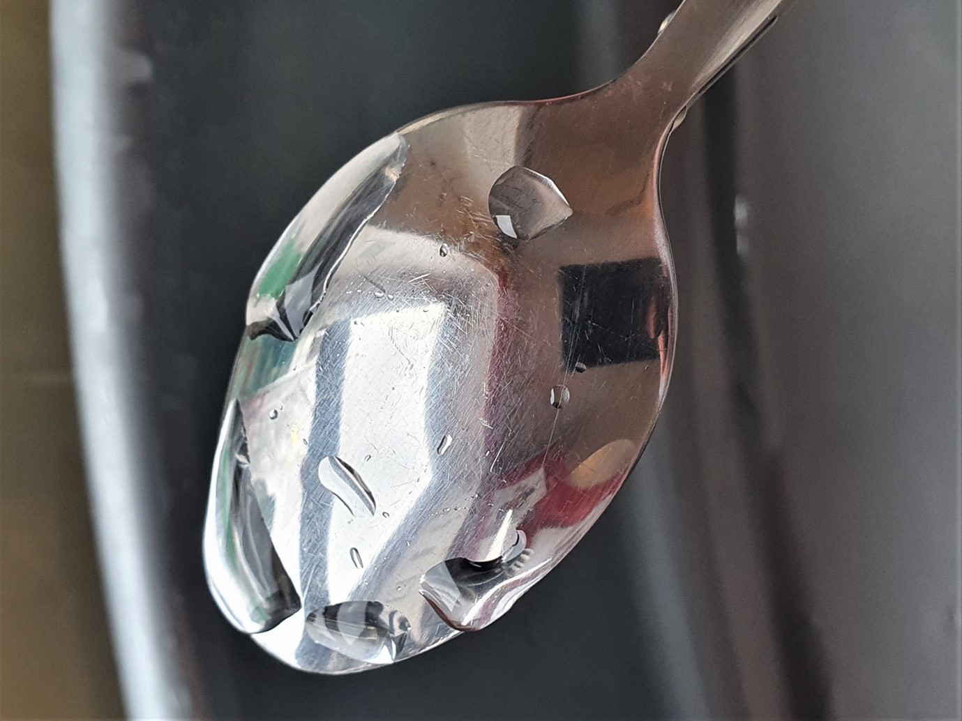 Metal spoon demonstrating the water break test, showing water beading up on the surface due to grease